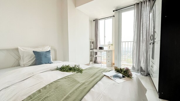 A bedroom with a bed, a desk, and a balcony with curtains.