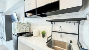 A modern kitchen with white tiles, a stainless steel sink, a black countertop, and a black hanging rack above the sink.