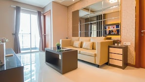 A modern living room with a sofa, a coffee table, a TV, and a bookshelf. - Modern And Spacious 2Br Apartment Green Bay Condominium (Jakarta)