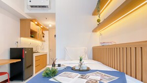 Une chambre d’hôtel compacte, dotée d’une kitchenette, d’un lit recouvert d’une courtepointe bleue et d’une tête de lit en bois.