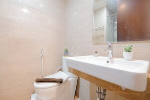A modern bathroom with a white toilet, a sink with a mirror above it, and a small potted plant on the sink. - Best Location And Homey Studio At Menteng Park Apartment (Jakarta)