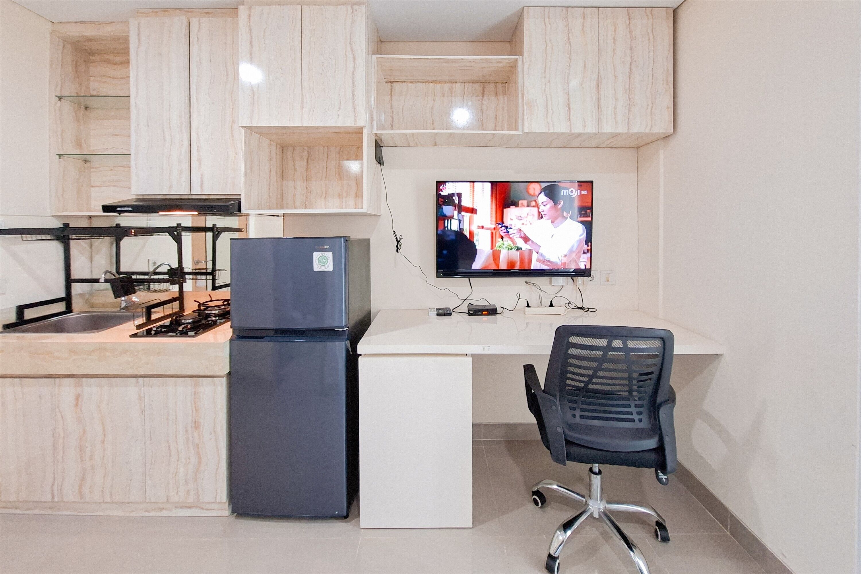A modern kitchen with a built-in gas stove, a refrigerator, and a flat-screen TV mounted on the wall.