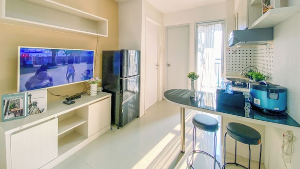 A modern kitchen with a built-in TV, a refrigerator, a coffee machine, and a bar area with stools. - 2Br Space Near Mall At Bassura City Apartment (Jakarta)