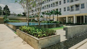 Un bâtiment moderne doté de nombreux balcons, d’une cour aménagée avec un élément décoratif aquatique et d’une grande variété de plantes.