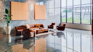 A modern lobby with a sofa set, two armchairs, a coffee table, and a large potted plant. - Cozy Studio Apartment At The Ayoma (South Tangerang)
