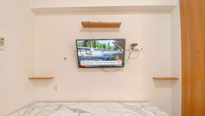 Una habitación con encimera de mármol, armarios de madera, un televisor montado mostrando un noticiero y un estante de madera encima del televisor.