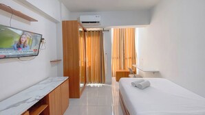 Habitación de hotel con televisor montado en la pared, cama con una toalla enrollada, armario de madera y equipo de aire acondicionado.