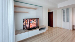 A modern living room with a flat-screen TV on a glass shelf, wooden beams on the ceiling, and a wooden floor. - 3Br Near Mall At Grand Sungkono Lagoon Apartment (Surabaya)