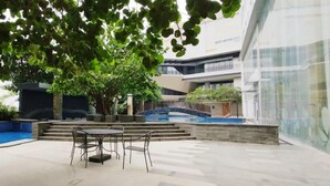 A modern outdoor area with a pool, a dining table with chairs, and a staircase leading to a building. - 3Br Near Mall At Grand Sungkono Lagoon Apartment (Surabaya)