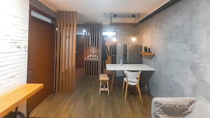 A compact room with a wooden floor, a white table, and a small stool. There is a door with a wooden panel and a mirror on the wall.