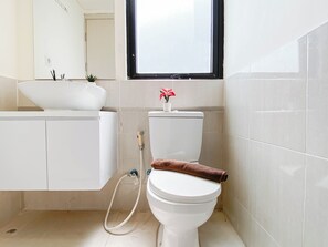 A bathroom with a white sink, a toilet, and a window above the toilet. - Compact Living 2Br At Meikarta Apartment (Cikarang)