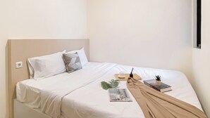 A neatly made bed with white bedding, a beige throw blanket, and a small potted plant.