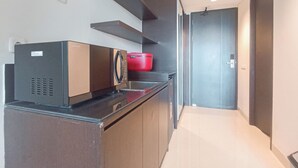 A modern kitchen with a built-in microwave, a red pot on the counter, and a door leading to another room. - Studio Apartment Skales Residence Near Waterblow Bali (Nusa Dua)