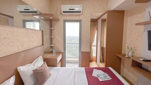 A hotel room with a bed, a bedside table, a mirror, a window, and an air conditioning unit. - Minimalist Studio (No Kitchen) At Tamansari Prospero Sidoarjo Apartment (Sidoarjo)