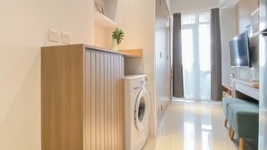 Une chambre d’hôtel moderne dotée d’une armoire en bois, d’un lave-linge, d’un téléviseur à écran plat et d’un coin salon avec un canapé vert.