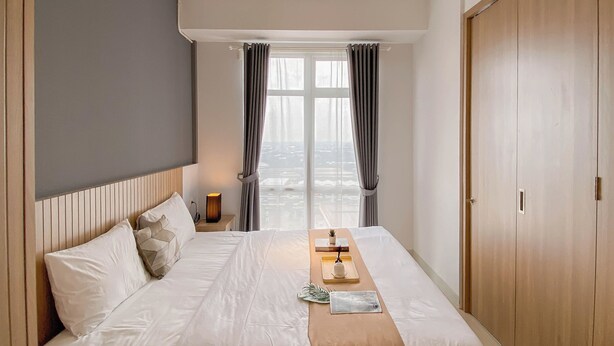Une chambre d’hôtel comprenant un lit, une table de chevet avec une lampe, une fenêtre avec des rideaux et une armoire.