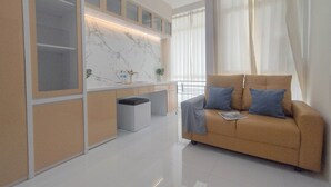 Una sala moderna con un sofá color beige, un salpicadero de mármol y un separador de vidrio.