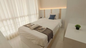 Una habitación de hotel moderna con una cama grande, una mesita de noche con una planta y una ventana con cortinas translúcidas.