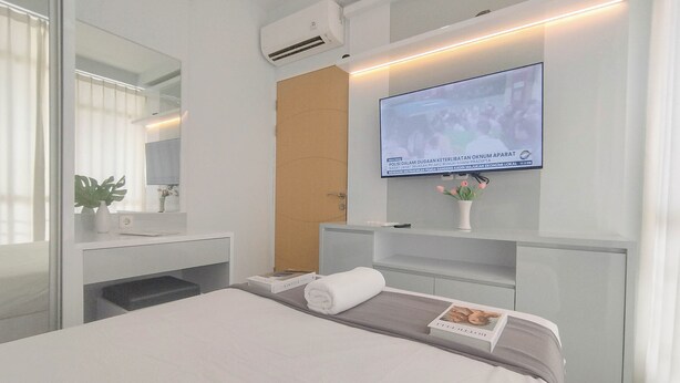 Una habitación de hotel moderna con una cama, un televisor montado en la pared, un pequeño escritorio con una planta y un espejo.