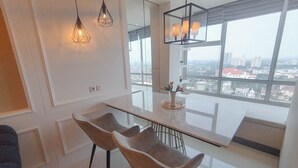 A modern kitchen with a large window, two pendant lights, and a dining area with two chairs. - Comfort 2Br Direct Access To Mall At Benson Supermall Mansion Apartment (Surabaya)