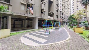 Un edificio residencial con varios balcones, un patio de recreo con estructuras esféricas de colores y un patio empedrado.