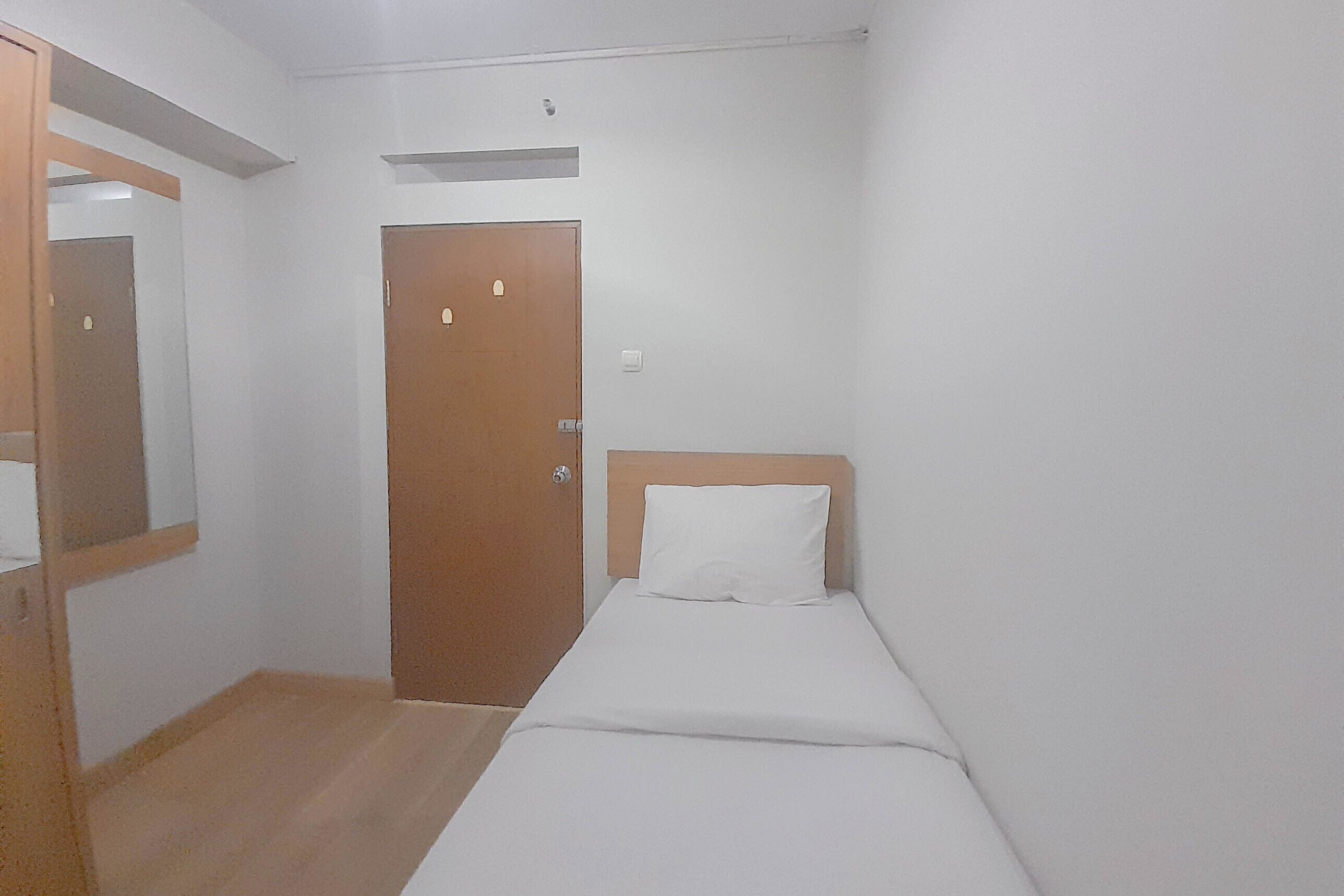A small, single-bed room with a wooden headboard, a wooden door, and a mirror on the left wall.