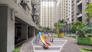 Un parque infantil con toboganes y estructuras de escalada en una zona residencial con edificios altos.