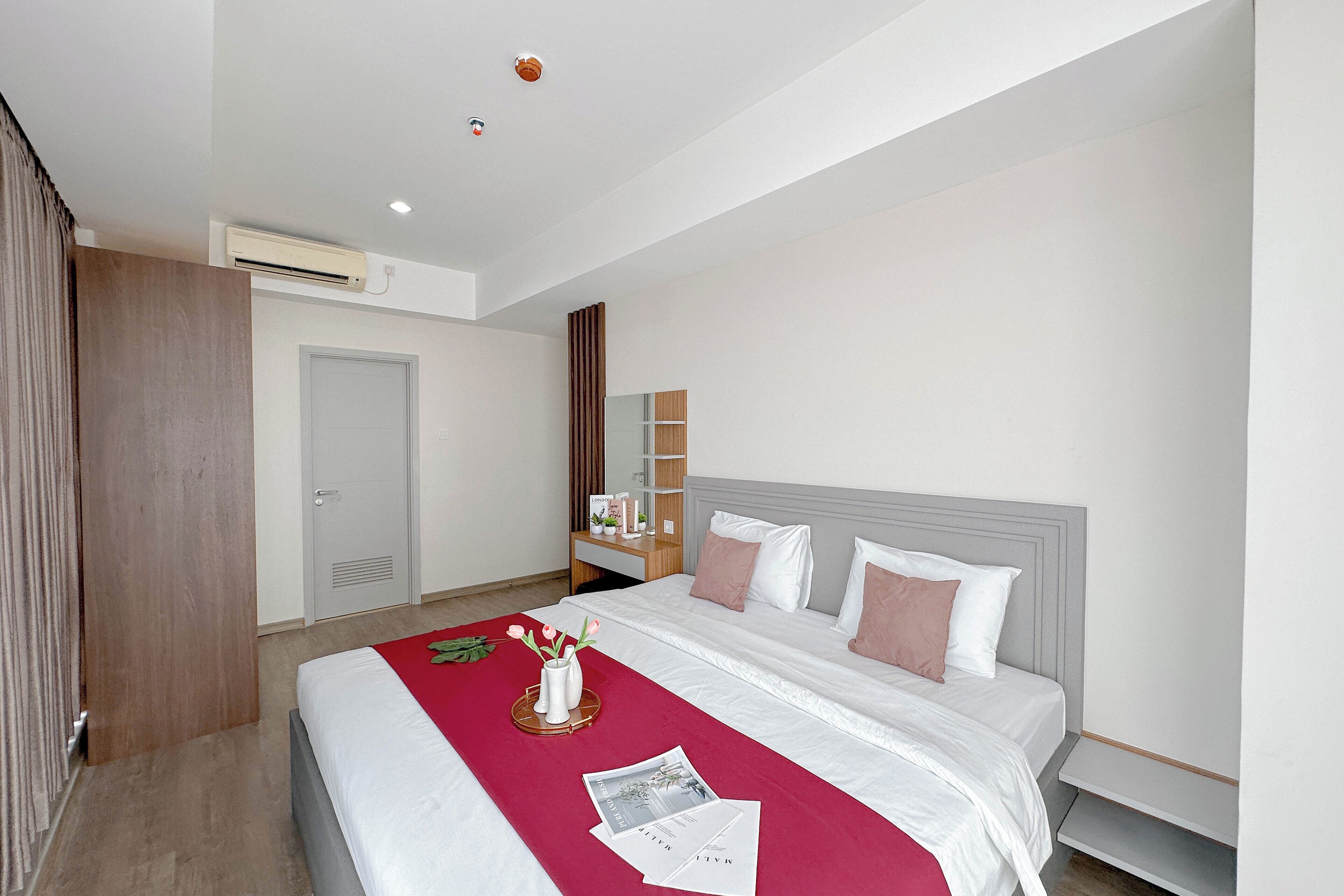 Une chambre d’hôtel moderne avec un lit bien fait, une armoire en bois, une table de chevet avec une lampe et un grand miroir au mur.