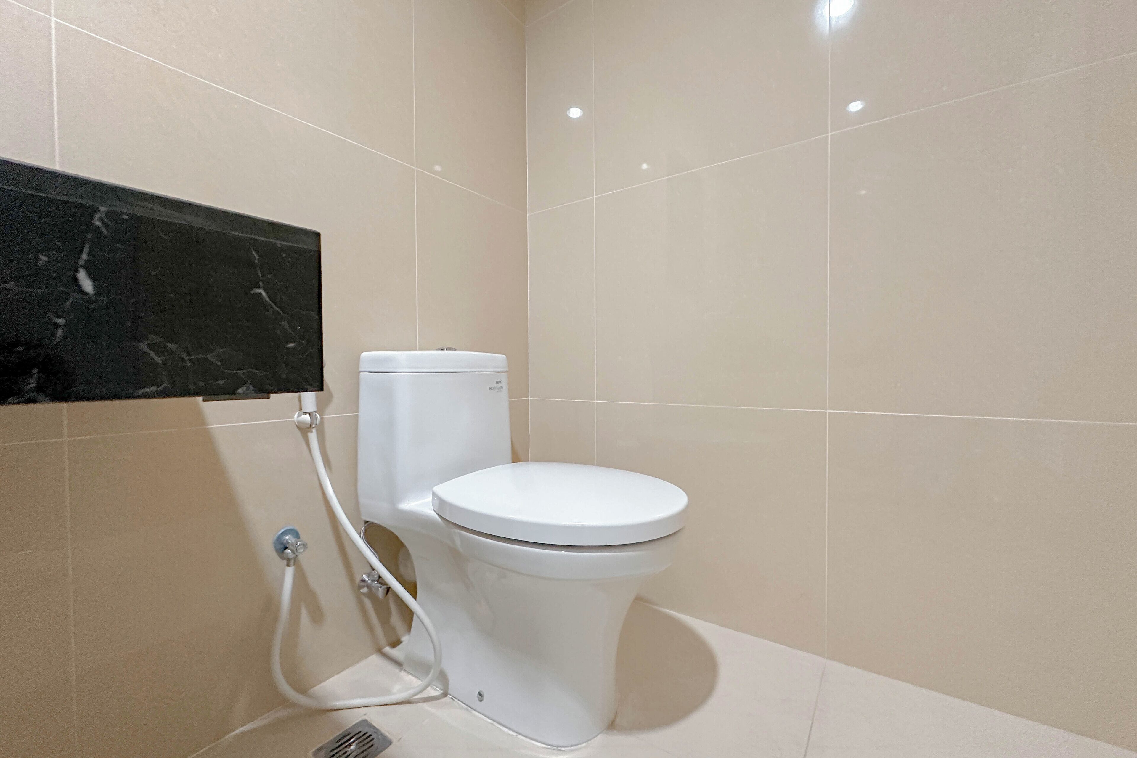 Une salle de bain moderne avec des toilettes blanches, un mur d’accent en marbre noir et des murs recouverts de carreaux beiges.