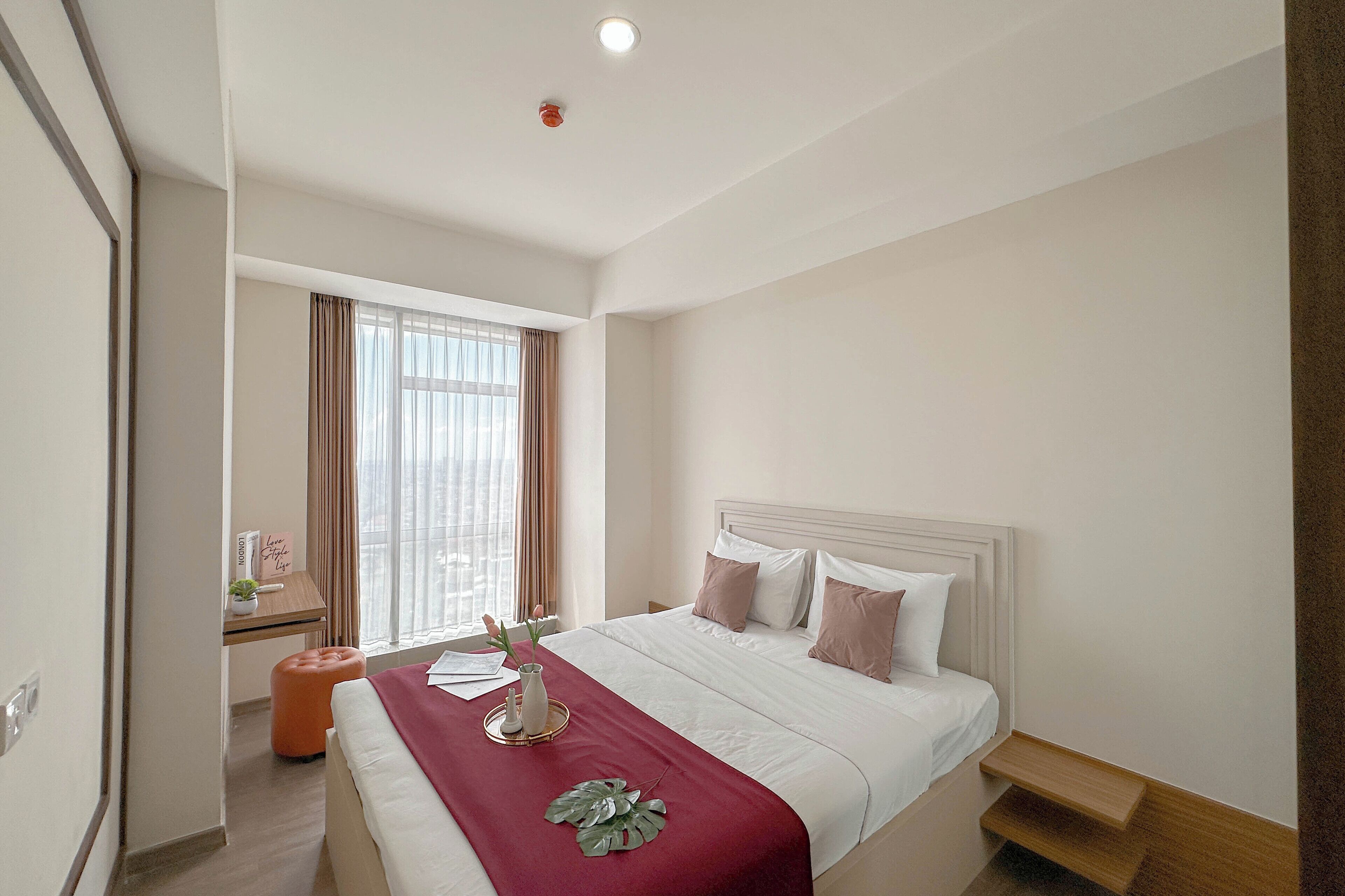 A hotel room with a bed, bedside table, and a window with curtains.