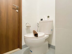 A bathroom with a white toilet, a wooden door, a towel on the toilet seat, and a small potted plant on the wall.