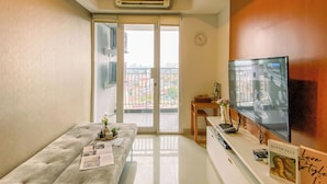 Una sala moderna con un sofá, un televisor de pantalla plana, una mesita con adornos y vistas de la ciudad a través de un ventanal.