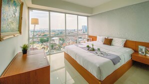 Habitación de hotel moderna con una cama grande, un escritorio y vistas a la ciudad a través de ventanas de techo a piso.