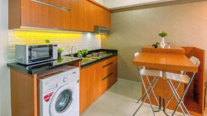 Cocina compacta con armarios de madera, microondas, lavadora y un pequeño comedor con mesa y sillas.