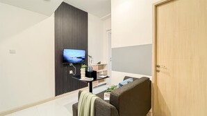 A modern living room with a flat-screen TV mounted on a dark panel, a wooden door, and a grey sofa. - Modern 2Br Apartment Near Tokyo Hub At Tokyo Riverside Pik 2 (Teluknaga)