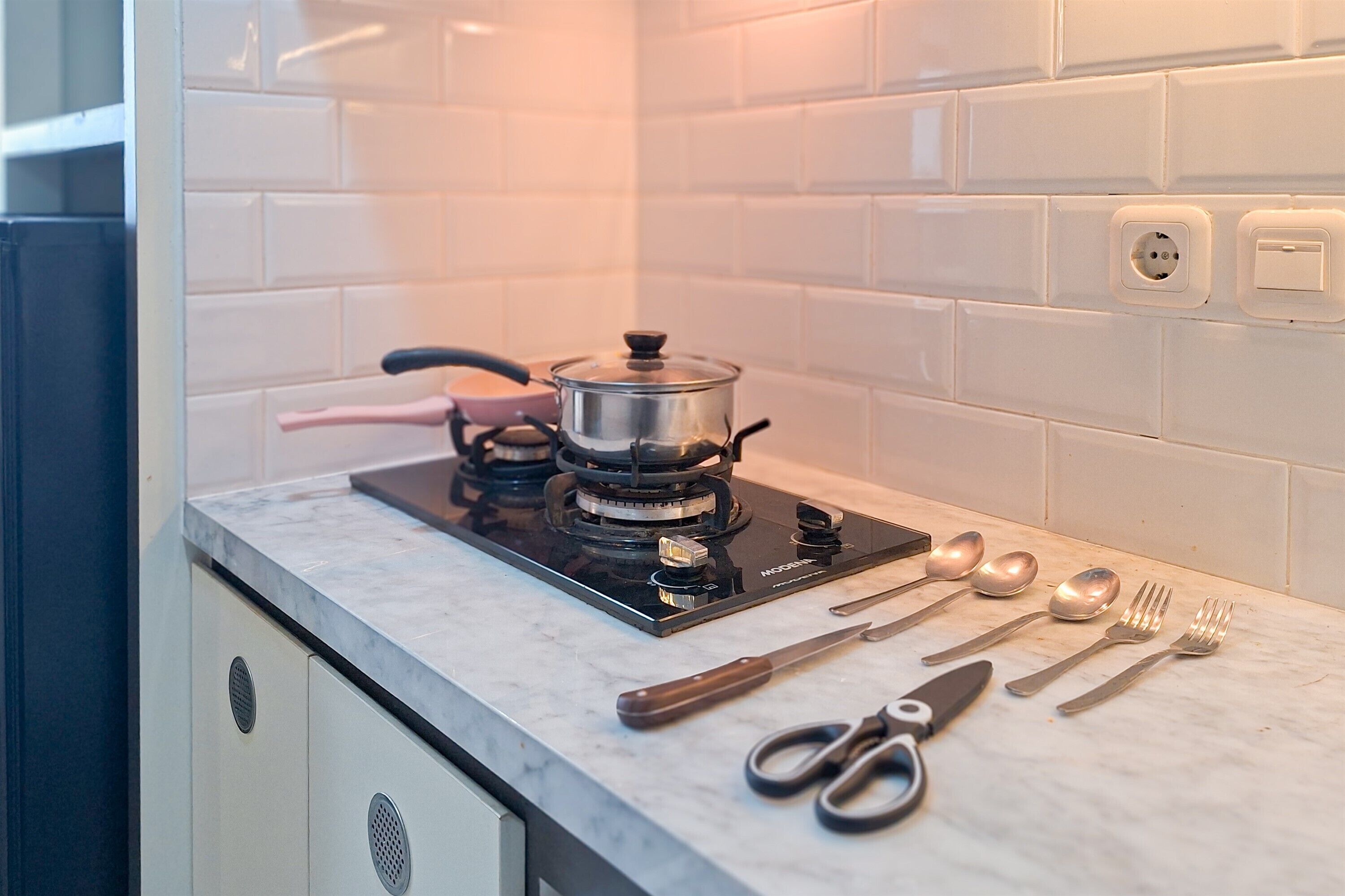 A kitchen with a gas stove, a pot on the burner, and various utensils like forks, spoons, and a knife on the counter.