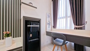 Une chambre d’hôtel moderne équipée d’un réfrigérateur intégré, d’un bureau avec une chaise, d’une fenêtre avec des rideaux et d’un tableau encadré au mur.
