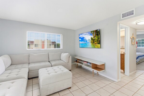 Un salon moderne avec un canapé d’angle, un téléviseur à écran plat fixé au mur et un petit meuble en bois pour la télévision.