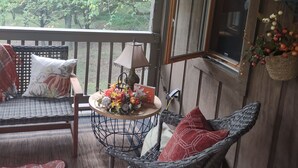 Een veranda met rieten meubels, een tafel met decoratieve objecten en uitzicht op bomen.