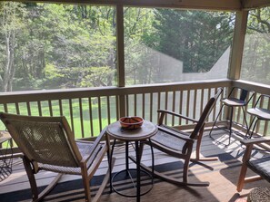 A covered outdoor area with a table and chairs, a bowl, and a view of a grassy area with trees.