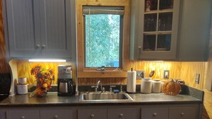 Een keuken met houten kastjes, een spoelbak, een koffiezetapparaat en een raam met uitzicht op bomen.