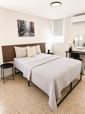 Une chambre moderne comprenant un lit, des tables de chevet, un bureau et un climatiseur fixé au mur.