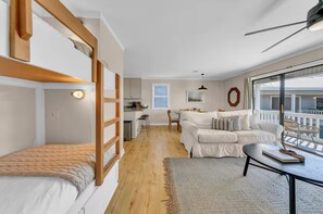 A modern apartment with a loft-style bedroom, a living area with a sofa and coffee table, and a kitchen in the background. - 30A Cozy Getaway - Steps to Sand! (Santa Rosa Beach)