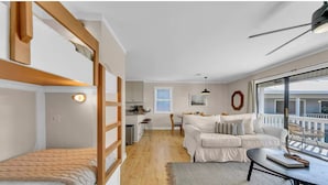 A modern apartment with a loft-style bedroom, a living area with a sofa and coffee table, and a kitchen in the background. - 30A Cozy Getaway - Steps to Sand! (Santa Rosa Beach)
