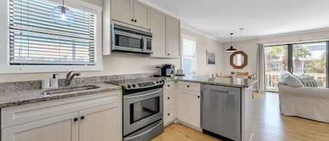 A modern kitchen with white cabinets, stainless steel appliances, and a wooden floor.