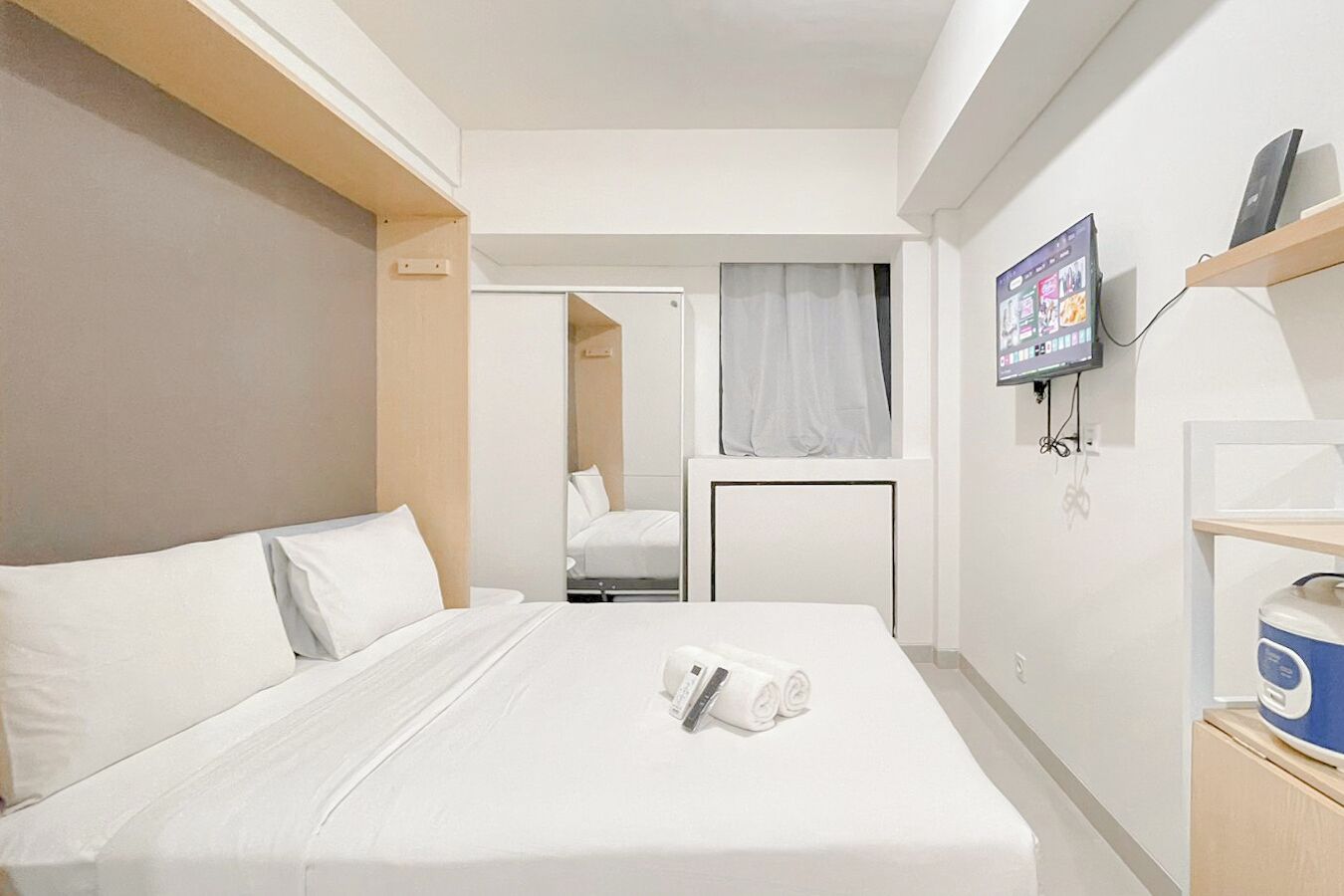 Habitación de hotel con cama, televisor montado en la pared y una mesita con una botella de agua.