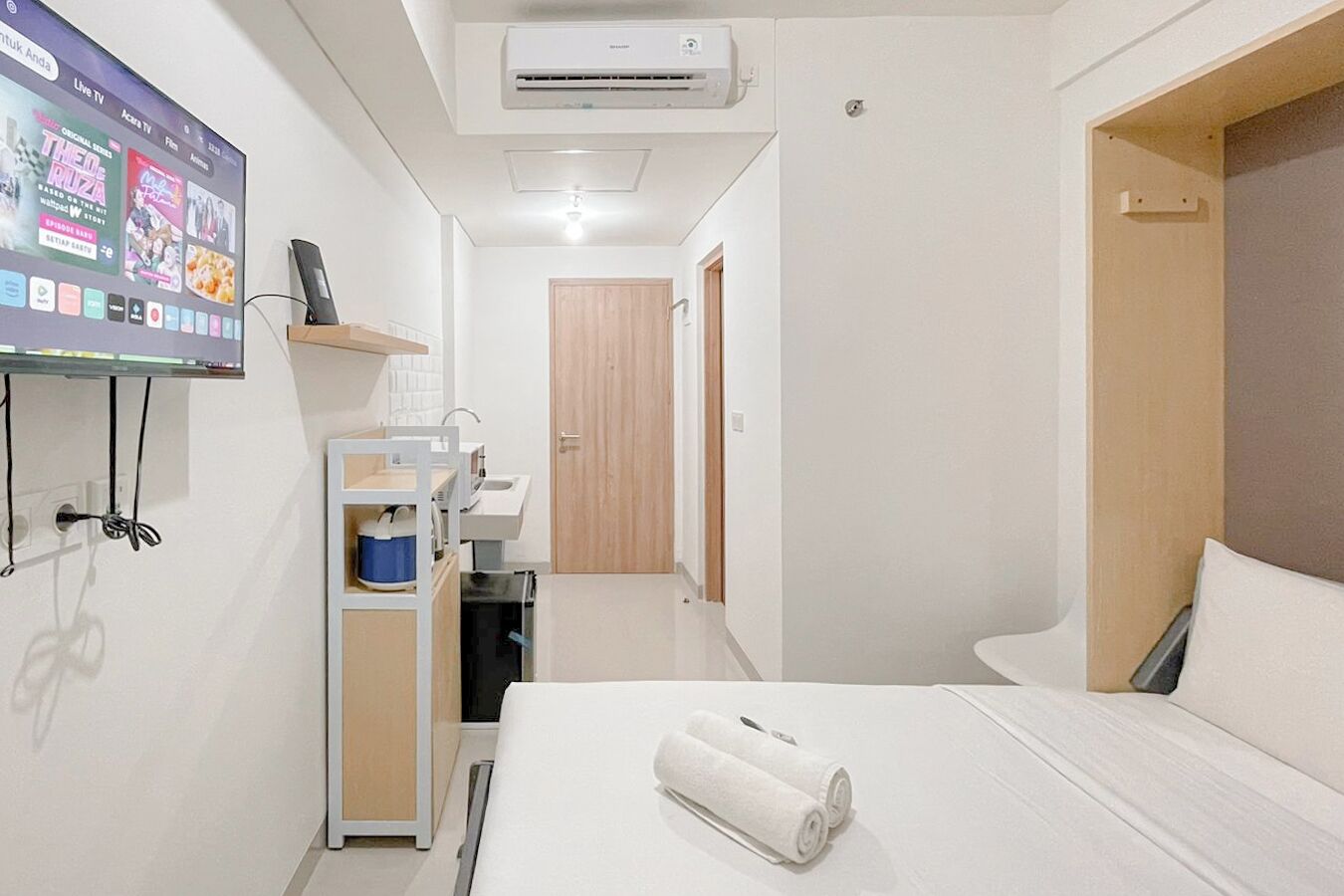 Een hotelkamer met een bed, een aan de muur bevestigde televisie, een kleine kitchenette en een houten deur.