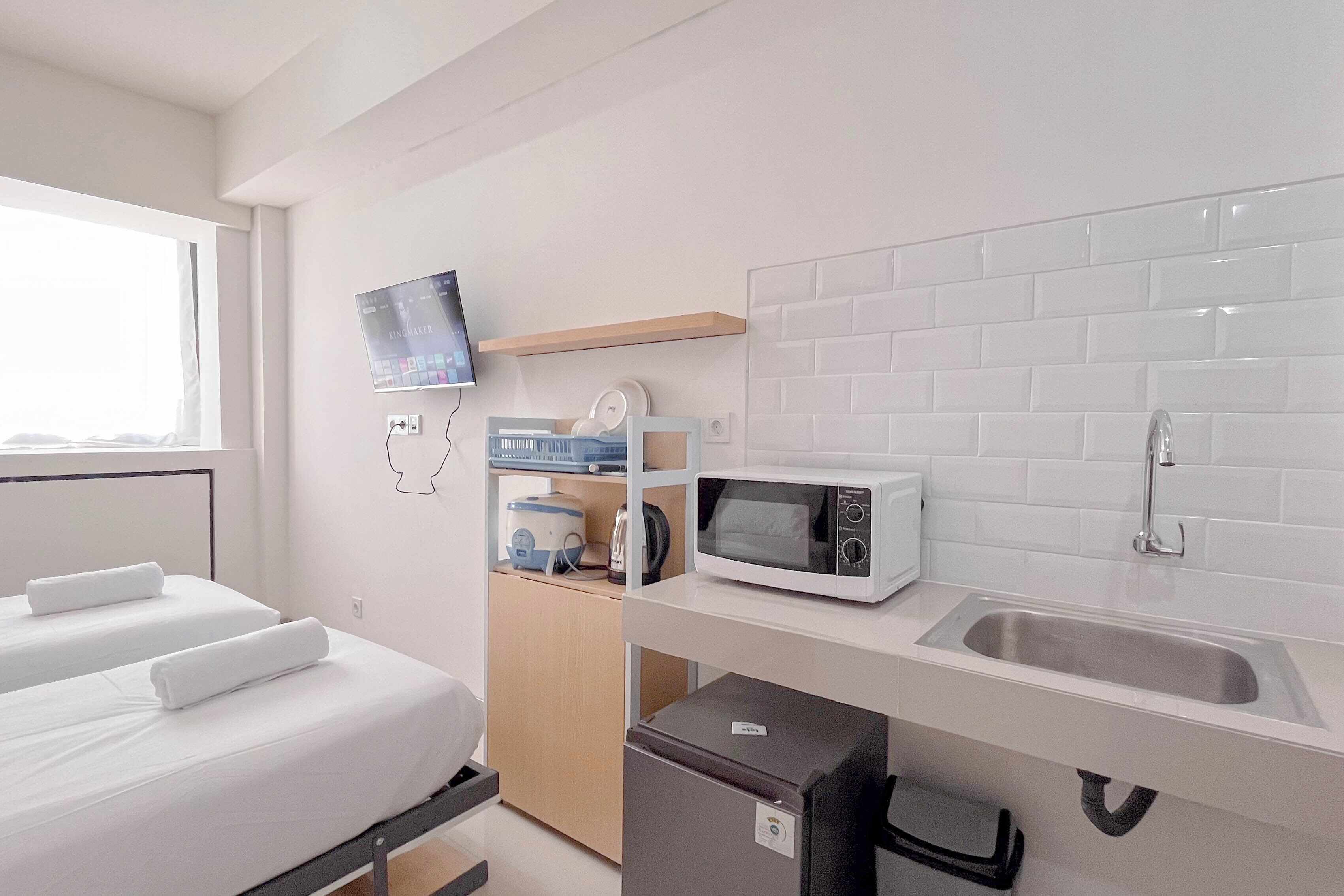 Une chambre d’hôtel compacte comprenant un lit, une petite kitchenette, un four à micro-ondes, un évier et un téléviseur fixé au mur.