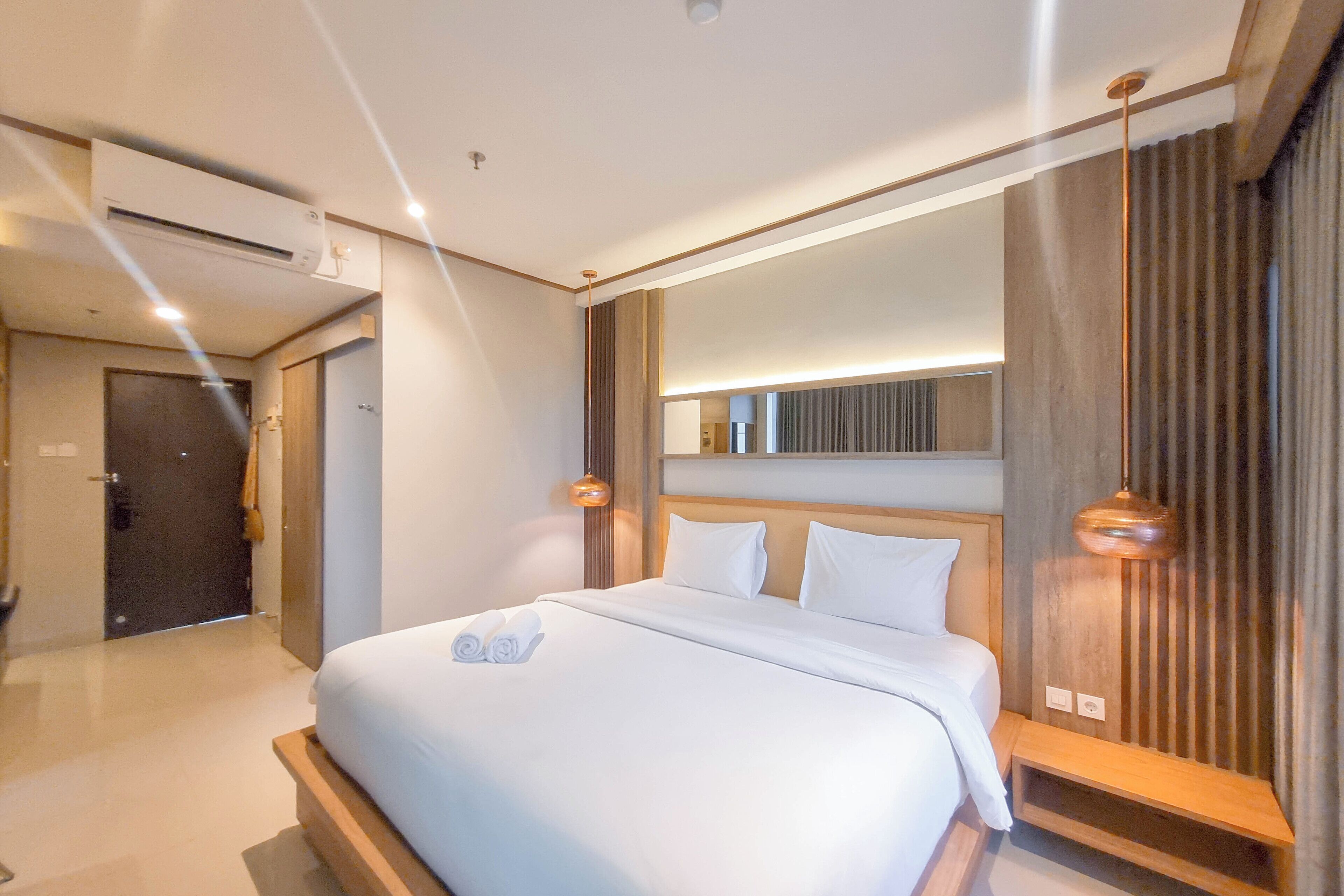 A modern hotel room with a large bed, a wooden headboard, and a built-in bench.