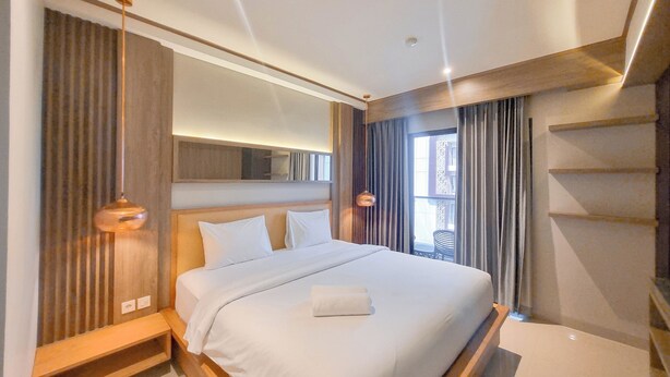 A modern hotel room with a large bed, built-in shelves, and a large window with curtains. - Warm And Minimalist Studio Apartment At Patraland Amarta (Ngaglik)